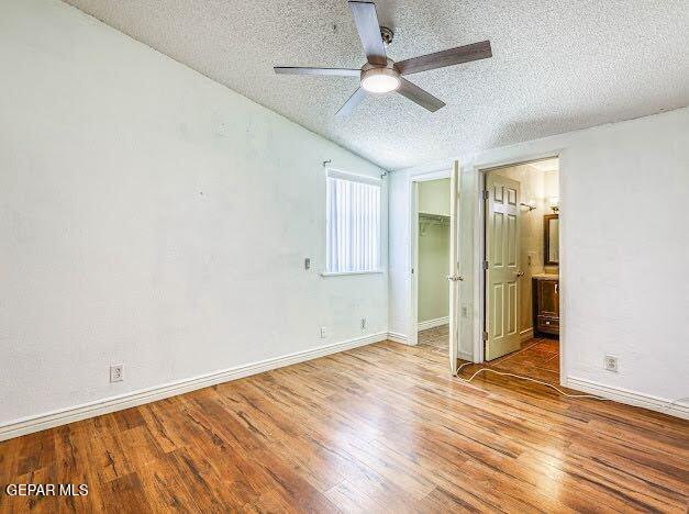 unfurnished bedroom with a textured ceiling, vaulted ceiling, wood finished floors, a closet, and a spacious closet
