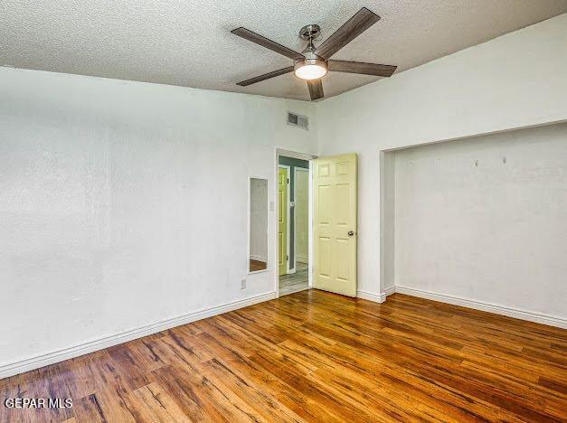 unfurnished bedroom with a textured ceiling, a ceiling fan, baseboards, wood finished floors, and visible vents