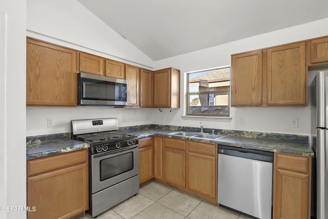 kitchen featuring dark countertops, a sink, appliances with stainless steel finishes, light tile patterned floors, and vaulted ceiling