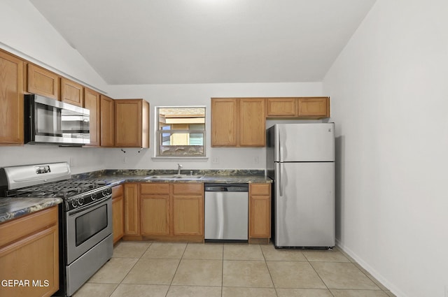 kitchen with dark countertops, a sink, appliances with stainless steel finishes, light tile patterned floors, and vaulted ceiling