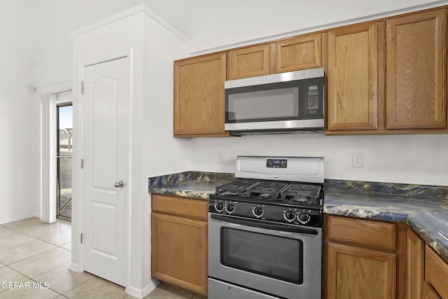 kitchen with light tile patterned floors, appliances with stainless steel finishes, baseboards, and brown cabinets