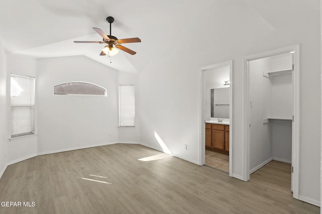 unfurnished bedroom with connected bathroom, light wood-style flooring, vaulted ceiling, a spacious closet, and a closet