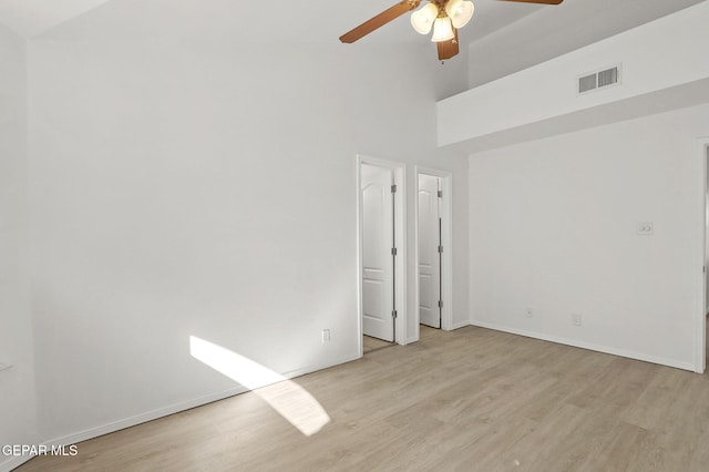 unfurnished bedroom featuring a ceiling fan, a towering ceiling, visible vents, wood finished floors, and baseboards