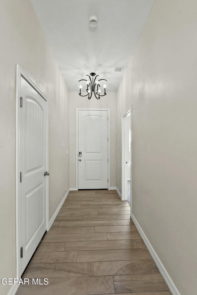 hall with an inviting chandelier, baseboards, wood finished floors, and visible vents