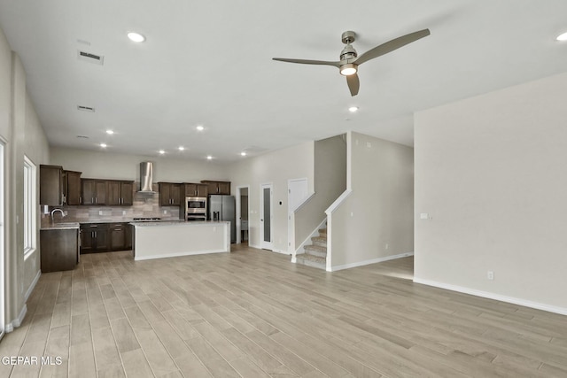unfurnished living room with stairs, a ceiling fan, baseboards, and light wood-style flooring