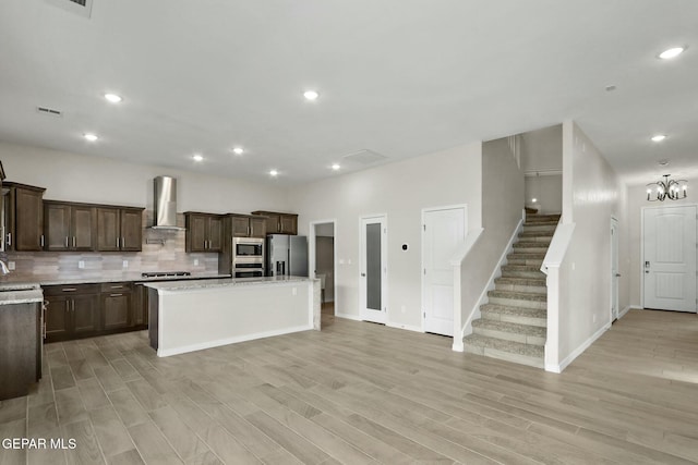 kitchen with wall chimney range hood, dark brown cabinets, stainless steel appliances, backsplash, and a kitchen island