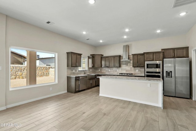 kitchen featuring wall chimney range hood, backsplash, visible vents, appliances with stainless steel finishes, and dark brown cabinets