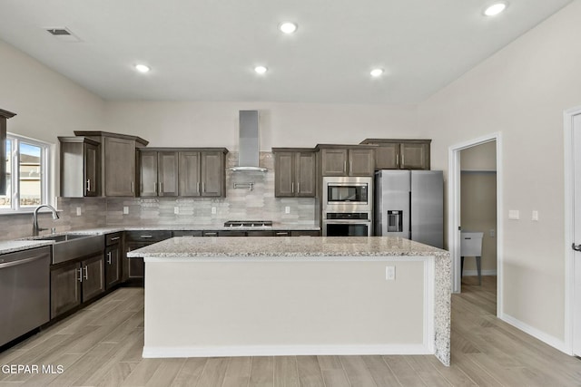 kitchen with a kitchen island, dark brown cabinets, wall chimney range hood, backsplash, and stainless steel appliances