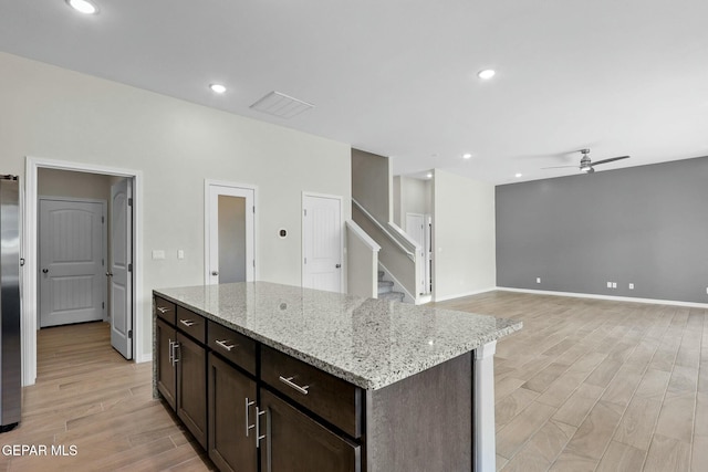 kitchen featuring a ceiling fan, light stone countertops, dark brown cabinets, freestanding refrigerator, and light wood-style floors