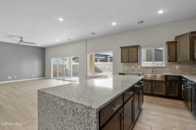 kitchen featuring light stone counters, a sink, decorative backsplash, a kitchen island, and visible vents