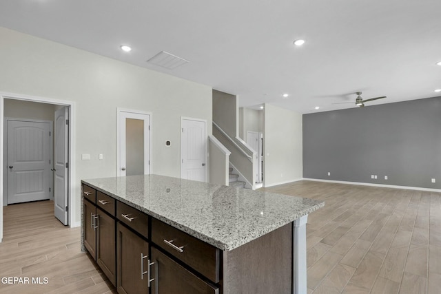 kitchen featuring a kitchen island, a ceiling fan, light stone countertops, dark brown cabinets, and light wood-style flooring