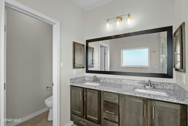 full bathroom featuring a sink, baseboards, toilet, and double vanity
