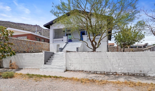 view of front of house featuring a porch, brick siding, fence, and stairway
