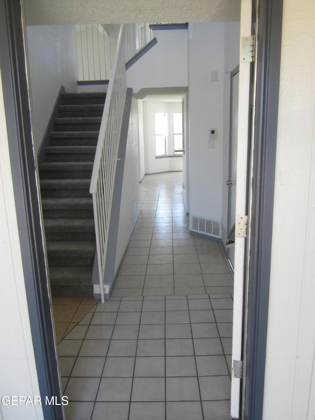 hall featuring visible vents, baseboards, light tile patterned flooring, and stairway