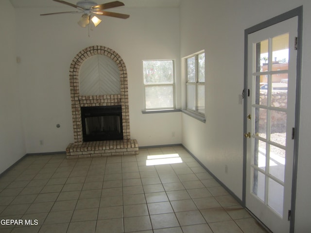 unfurnished living room with a brick fireplace, light tile patterned flooring, a wealth of natural light, and ceiling fan