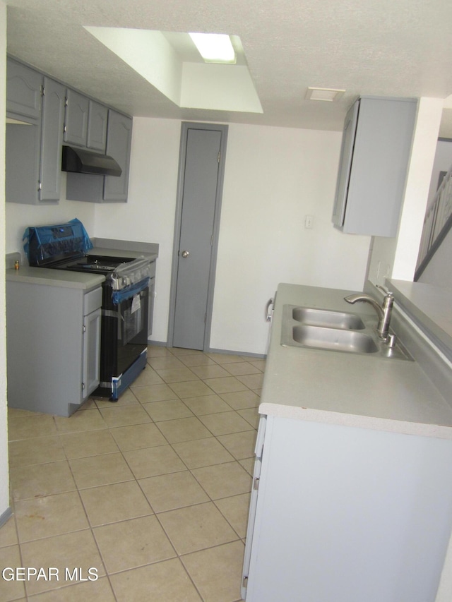 kitchen featuring a sink, gas stove, light countertops, light tile patterned floors, and under cabinet range hood