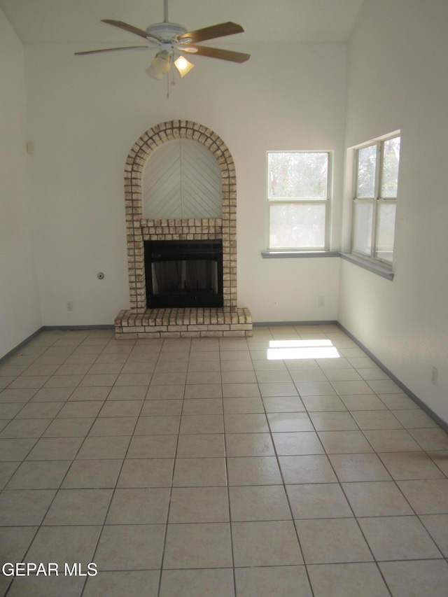 unfurnished living room with baseboards, ceiling fan, a brick fireplace, and light tile patterned flooring