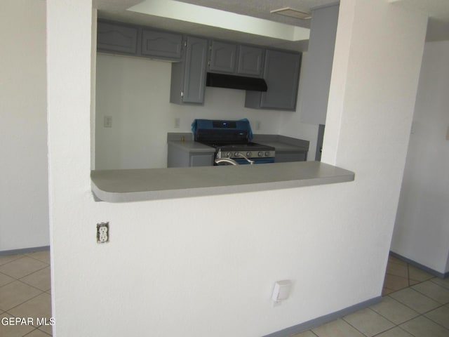 kitchen featuring a peninsula, baseboards, light tile patterned floors, gas range, and under cabinet range hood
