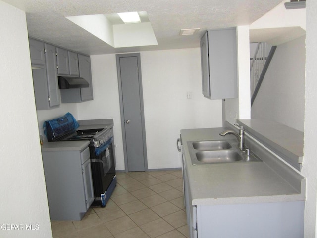kitchen with range with gas stovetop, light tile patterned flooring, gray cabinets, under cabinet range hood, and a sink