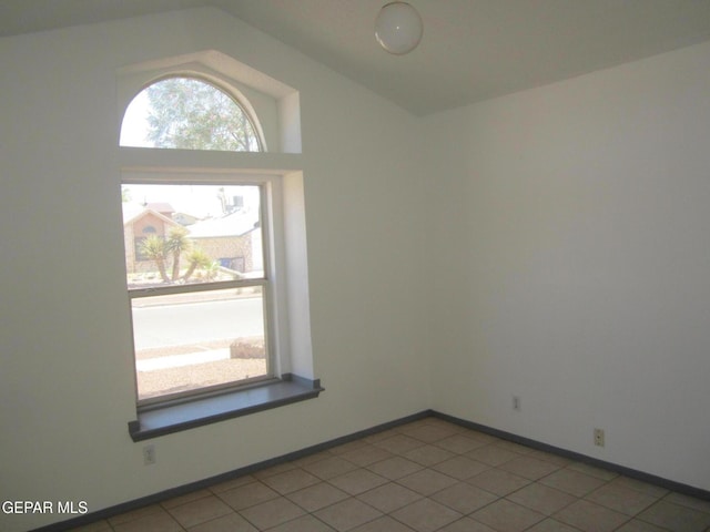 spare room featuring baseboards, light tile patterned floors, and lofted ceiling