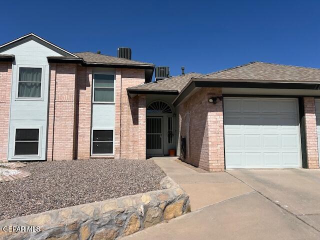 tri-level home featuring roof with shingles, a garage, central air condition unit, brick siding, and concrete driveway