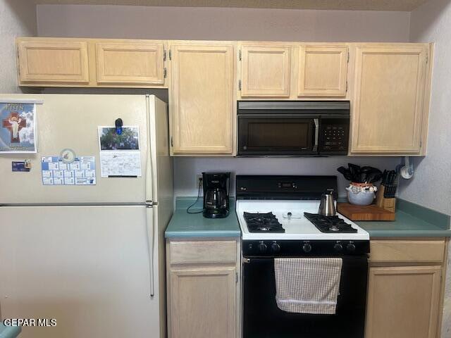 kitchen featuring range with gas cooktop, black microwave, light brown cabinetry, light countertops, and freestanding refrigerator