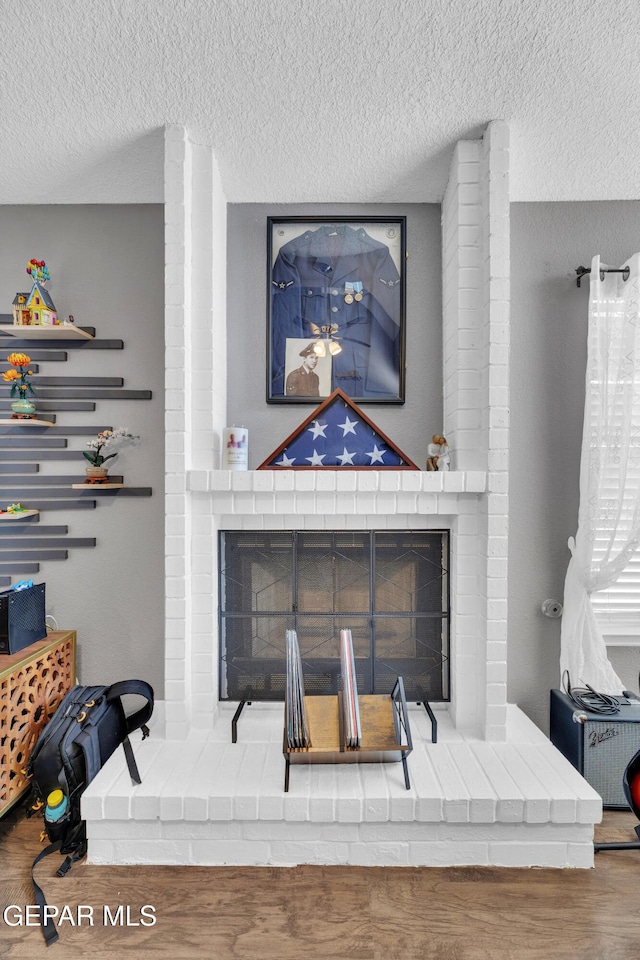 interior details with a brick fireplace, a textured ceiling, and wood finished floors