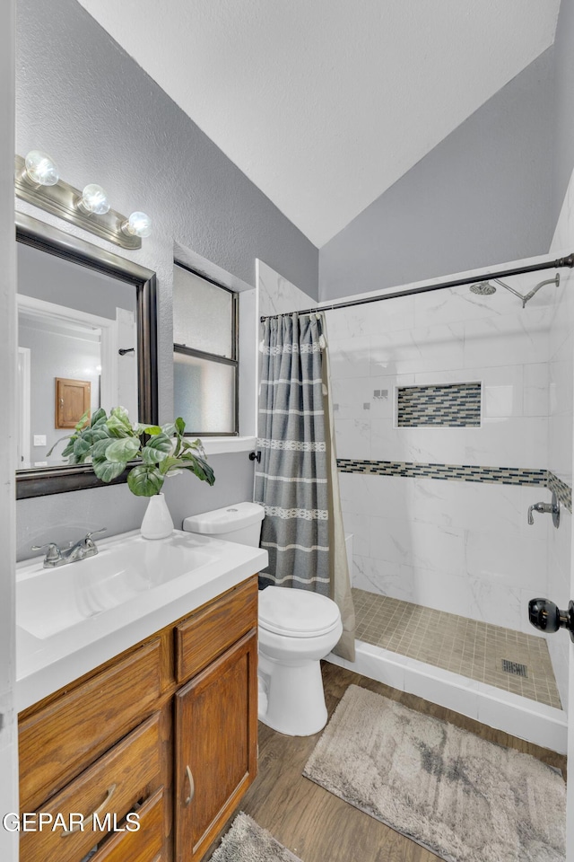 bathroom with wood finished floors, vanity, toilet, lofted ceiling, and tiled shower