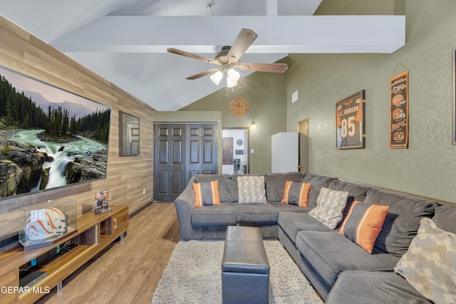 living room with vaulted ceiling with beams, light wood-style flooring, ceiling fan, and a textured wall