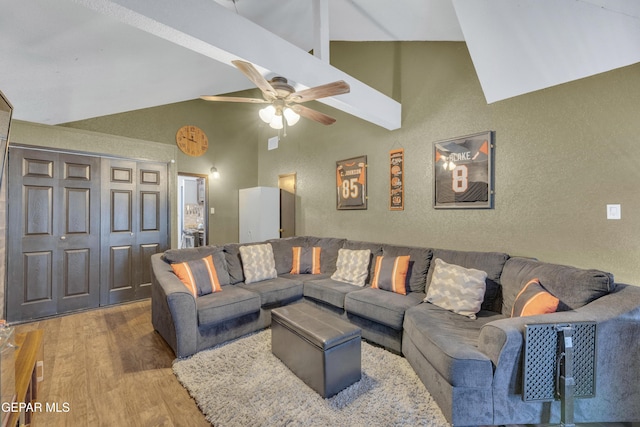 living area featuring a textured wall, ceiling fan, wood finished floors, and high vaulted ceiling