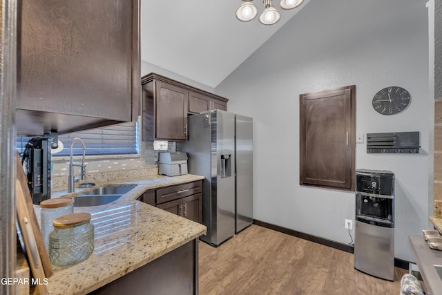 kitchen with dark brown cabinetry, stainless steel refrigerator with ice dispenser, vaulted ceiling, a sink, and light wood-style floors
