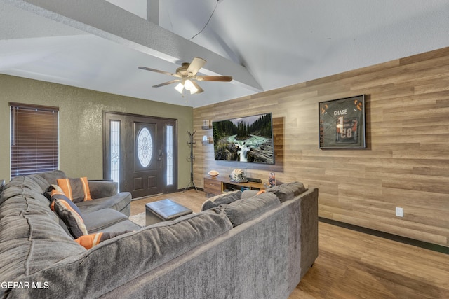 living room featuring ceiling fan, vaulted ceiling, wood walls, wood finished floors, and a textured wall