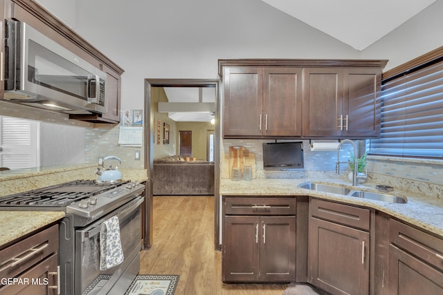 kitchen with light wood-style floors, a sink, backsplash, vaulted ceiling, and stainless steel appliances