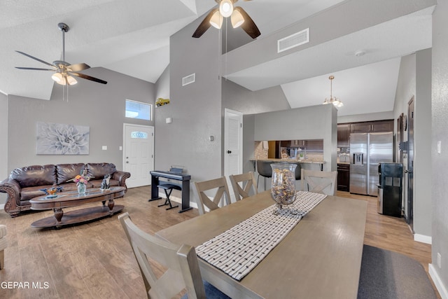 dining area featuring light wood-type flooring, a ceiling fan, visible vents, and high vaulted ceiling