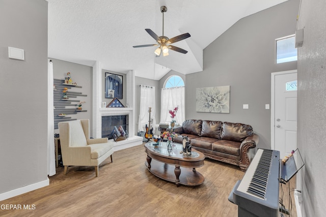 living room featuring a ceiling fan, wood finished floors, high vaulted ceiling, baseboards, and a fireplace with raised hearth