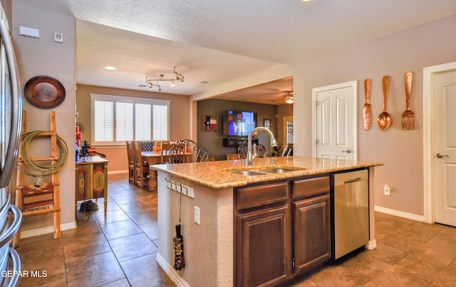 kitchen featuring stainless steel dishwasher, light tile patterned flooring, an island with sink, and a sink