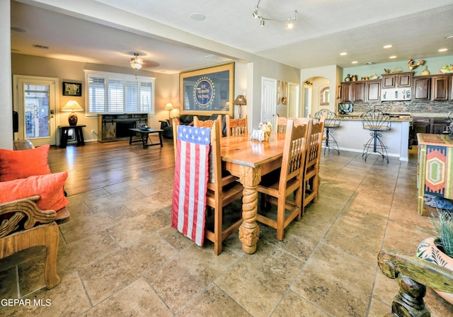 dining space with a ceiling fan, visible vents, arched walkways, baseboards, and stone tile floors