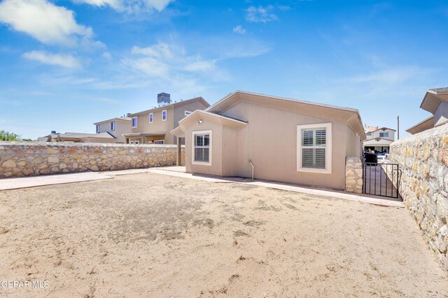 back of house featuring fence, a chimney, a gate, and stucco siding