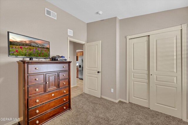 bedroom with light carpet, baseboards, stainless steel refrigerator with ice dispenser, visible vents, and a closet