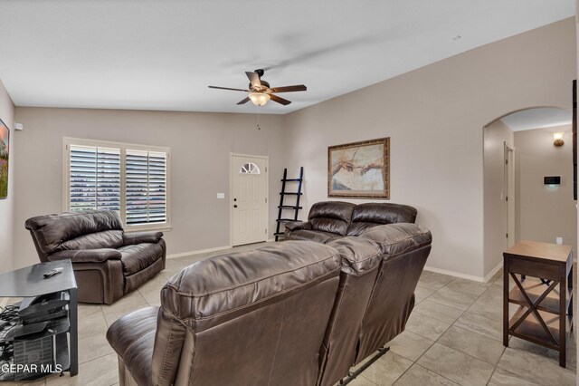 living area with light tile patterned floors, arched walkways, baseboards, and a ceiling fan