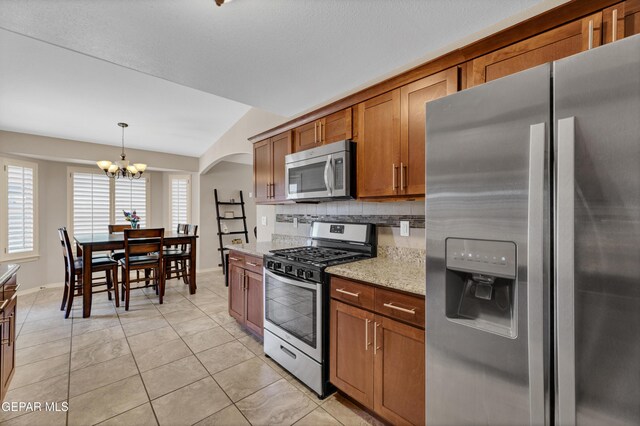 kitchen featuring an inviting chandelier, brown cabinets, arched walkways, vaulted ceiling, and stainless steel appliances