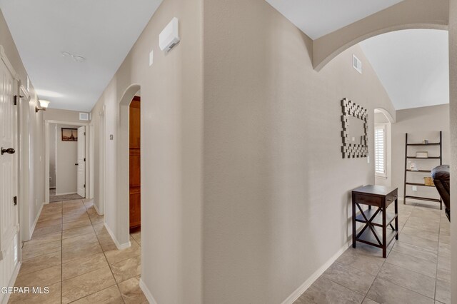 corridor with arched walkways, baseboards, visible vents, and light tile patterned floors