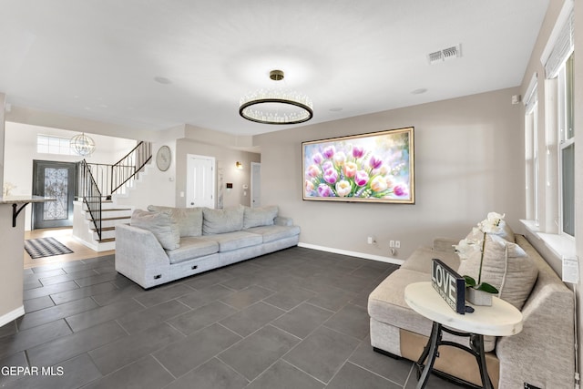 living area featuring baseboards, stairs, a chandelier, and visible vents