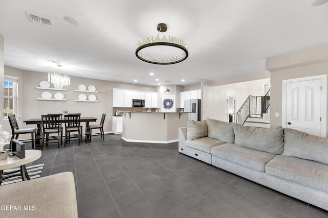 living area with visible vents, dark tile patterned floors, stairway, and an inviting chandelier