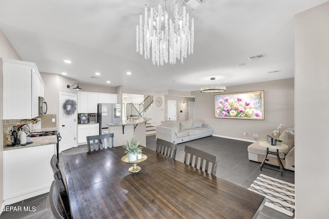 dining area featuring visible vents, a notable chandelier, stairway, and dark tile patterned flooring