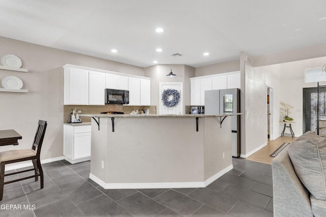 kitchen with white cabinets, black microwave, a kitchen breakfast bar, a center island, and visible vents