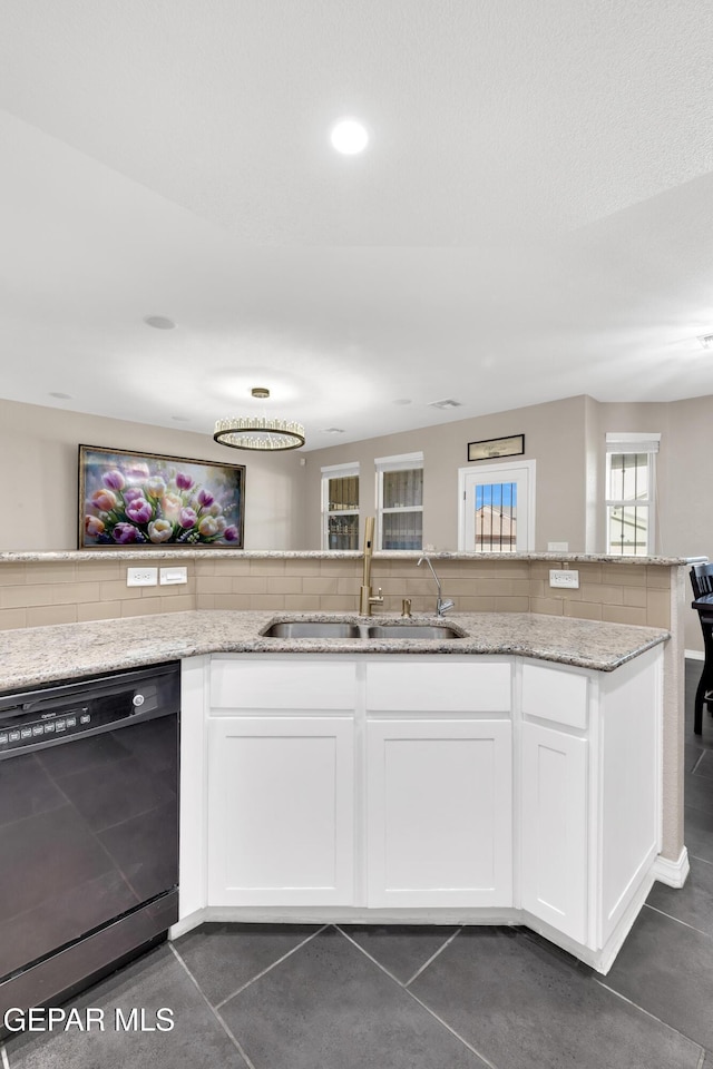 kitchen featuring dishwasher, a sink, light stone counters, dark tile patterned flooring, and white cabinetry