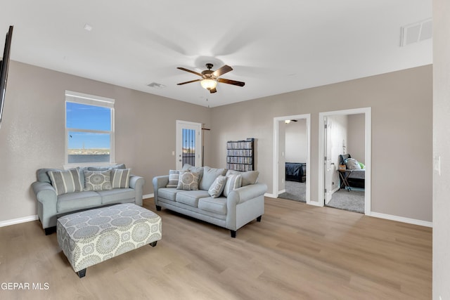 living area with baseboards, a ceiling fan, light wood finished floors, and visible vents