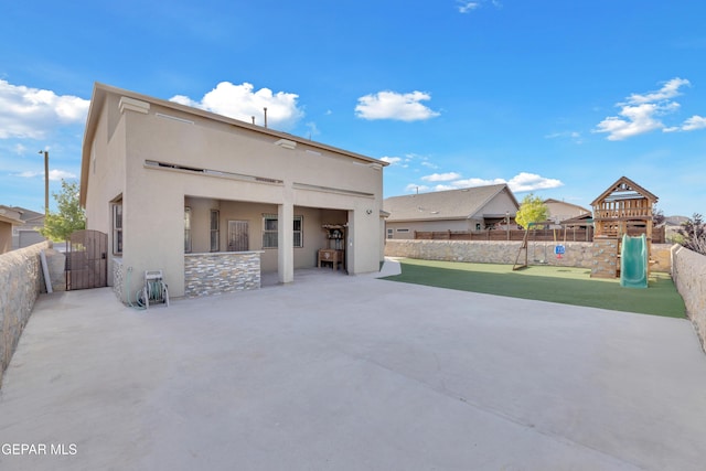 rear view of house featuring a gate, fence, a playground, a patio, and stucco siding