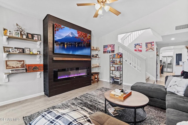 living room with stairs, wood finished floors, a fireplace, baseboards, and a ceiling fan